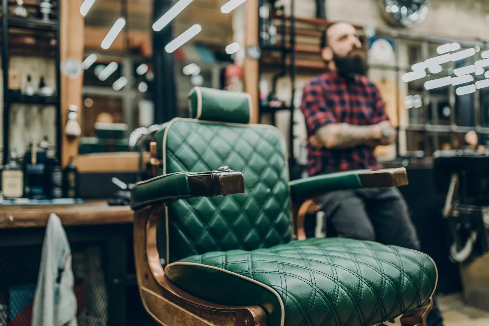 Barber seated beside a green leather barber chair in a classic barbershop