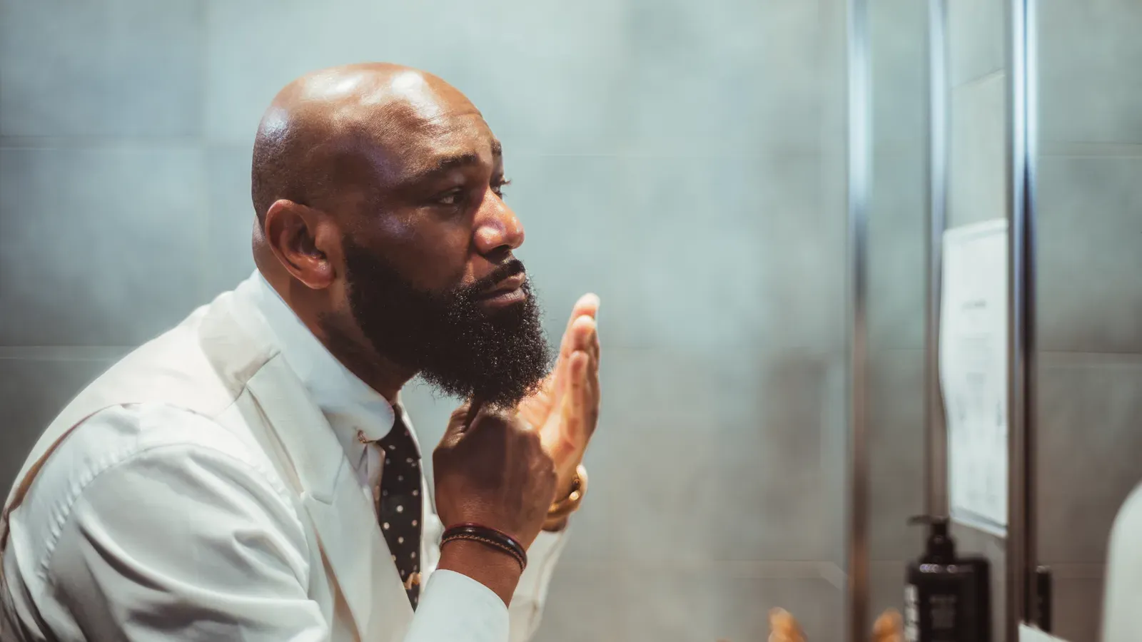 Well-groomed bearded man checking his beard in a barbershop mirror