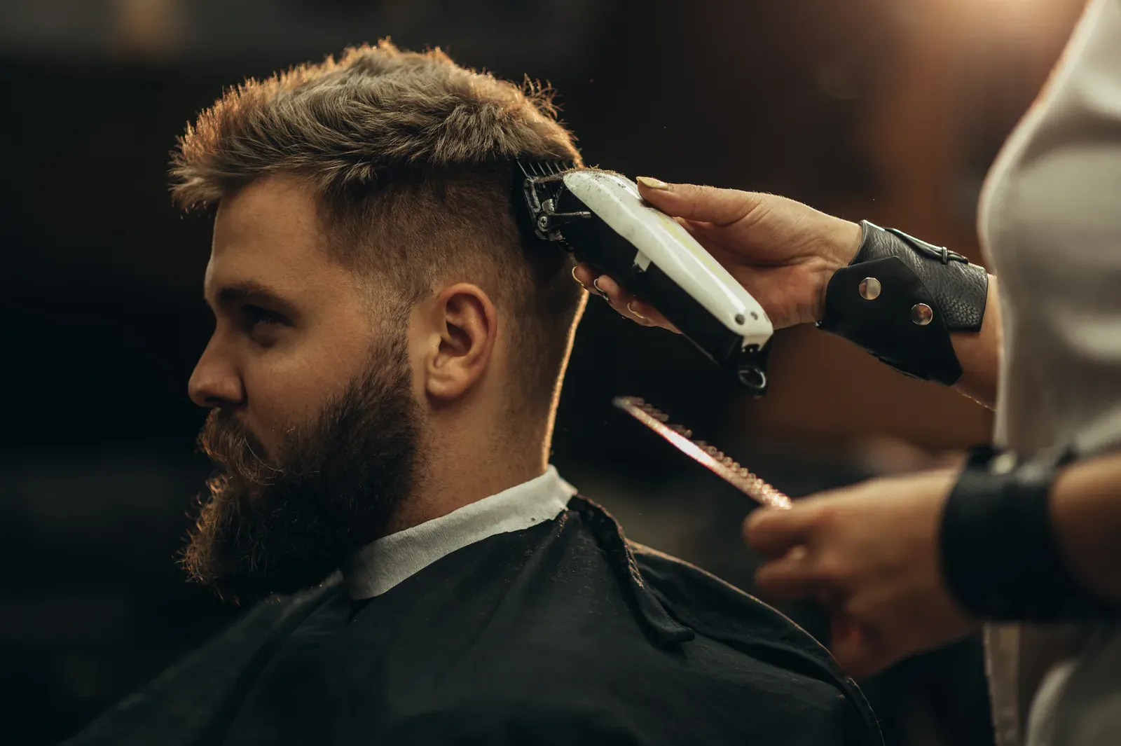 Barber shaping a skin fade on a bearded client with clippers