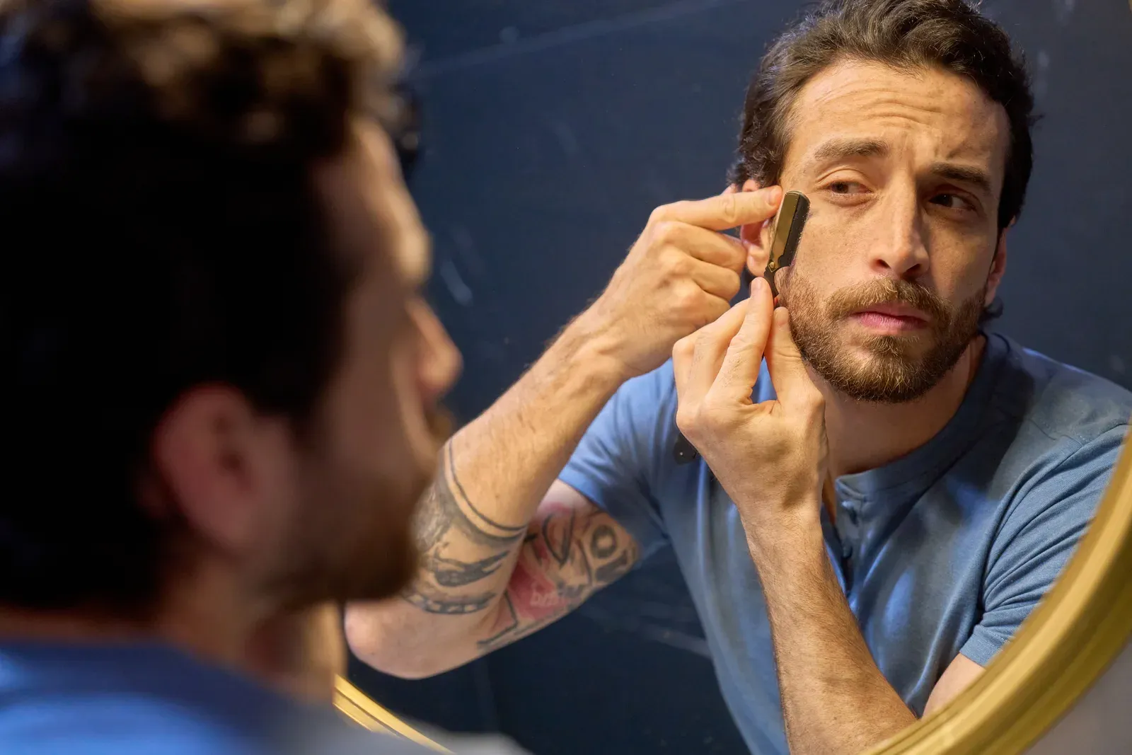 Man trimming his beard in a mirror at home