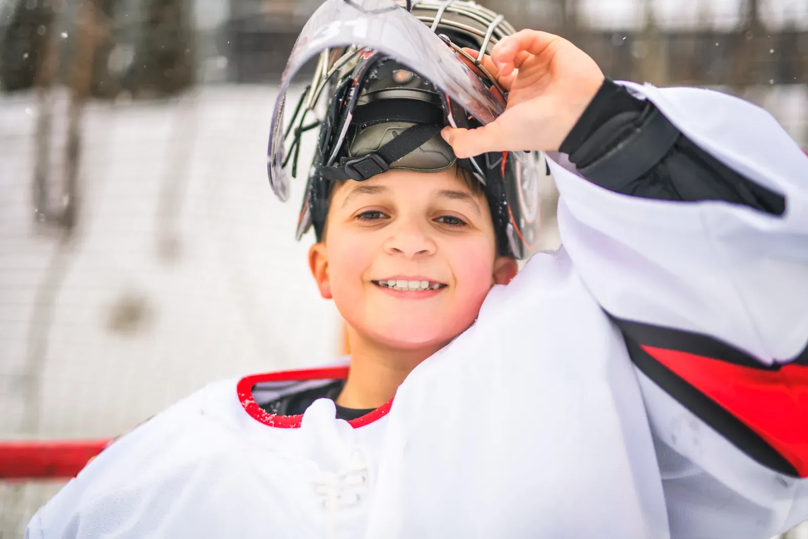 Young hockey player in a helmet smiling at an outdoor rink