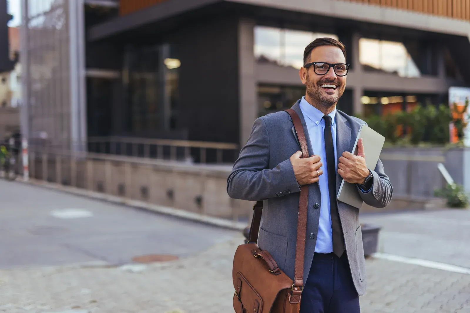 Man with glasses, a trimmed beard and a briefcase outside an office building