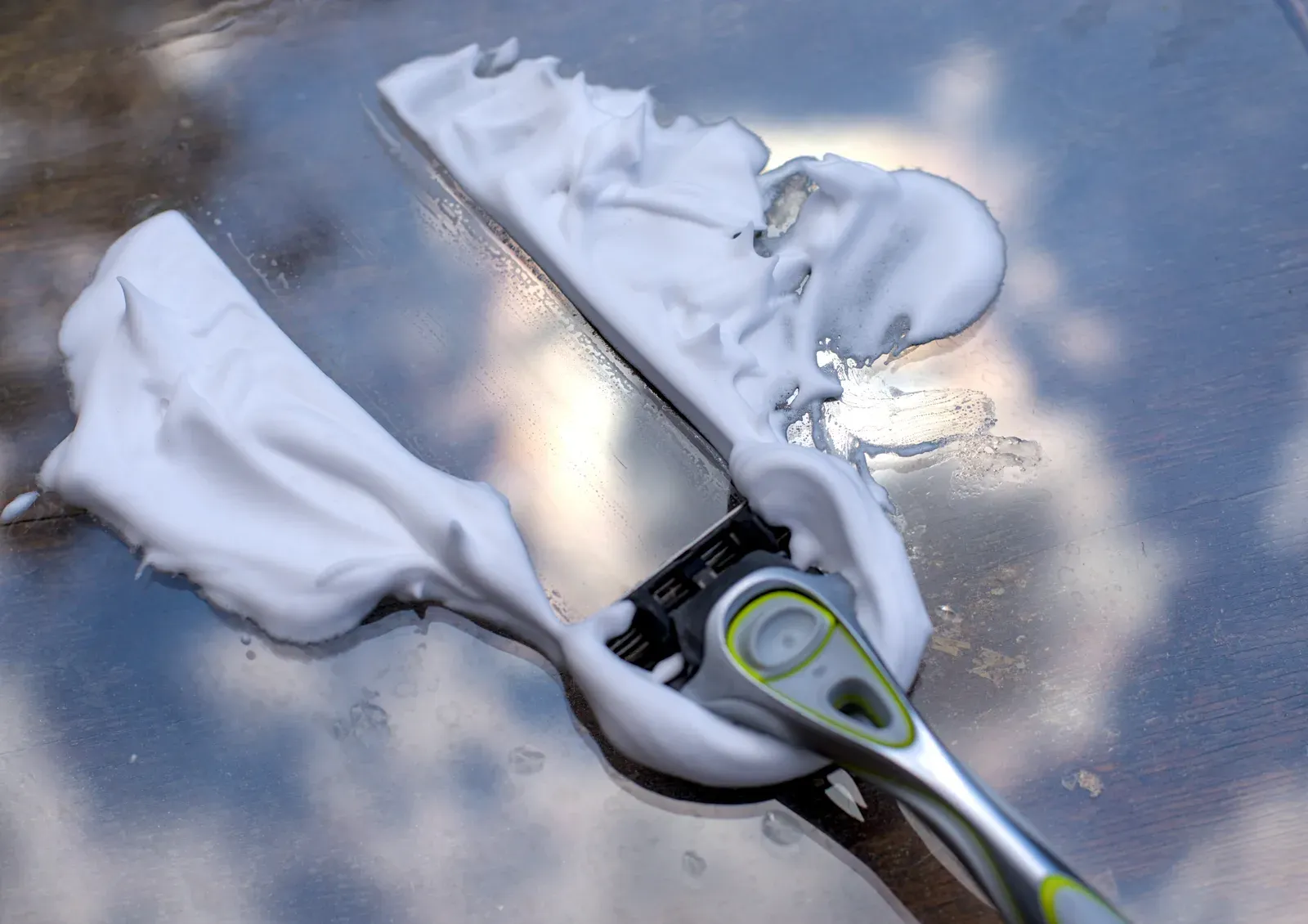 Safety razor and shaving foam on a glass surface