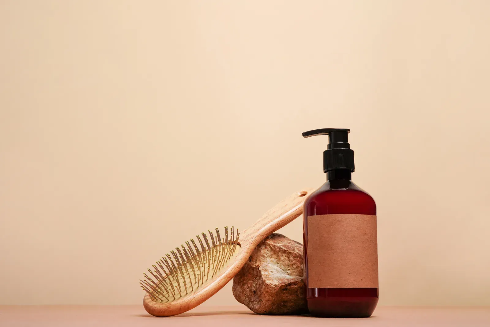Amber pump bottle of shampoo beside a wooden hair brush